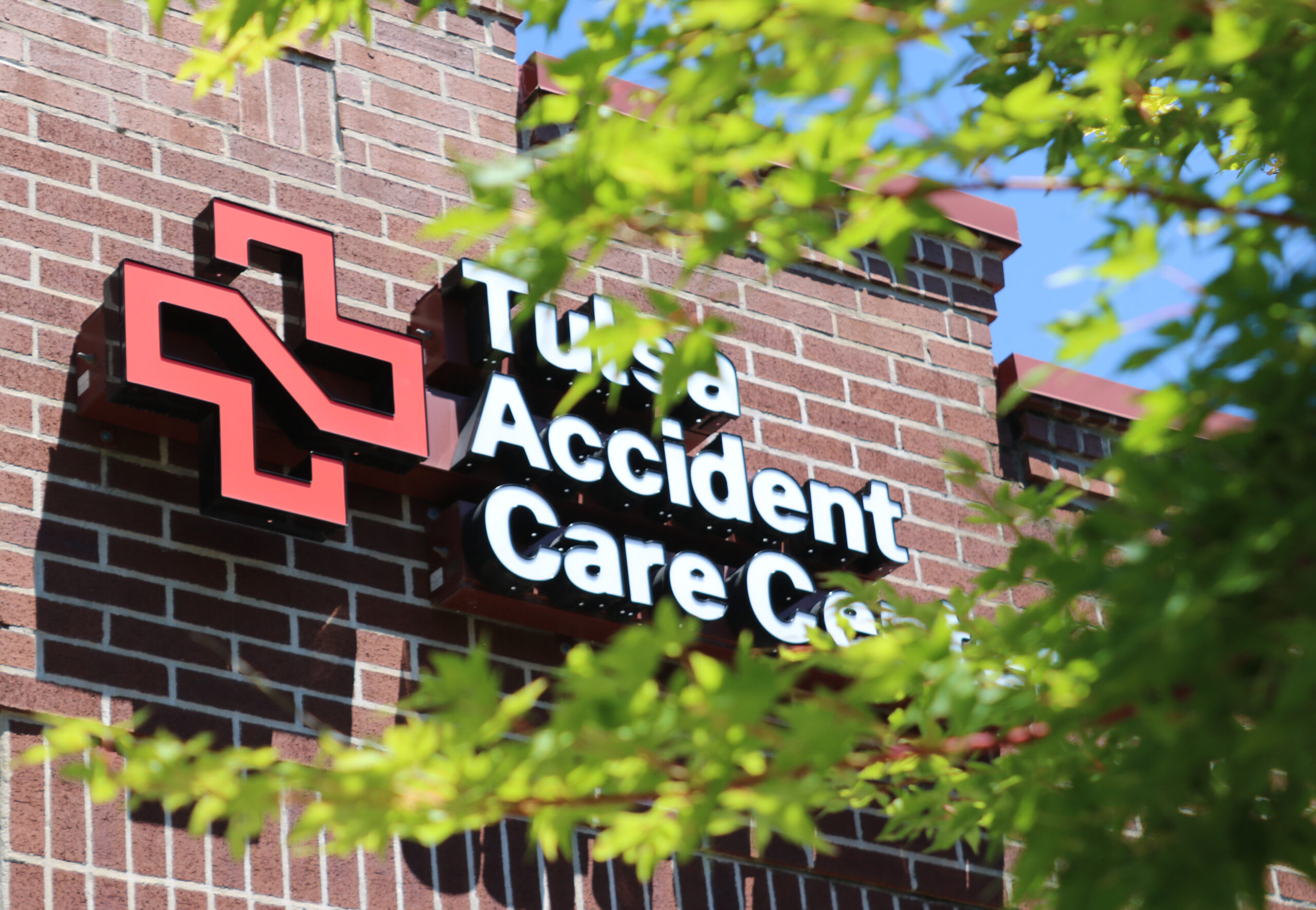 Exterior signage of Tulsa Accident Care Center as seen through tree branches.